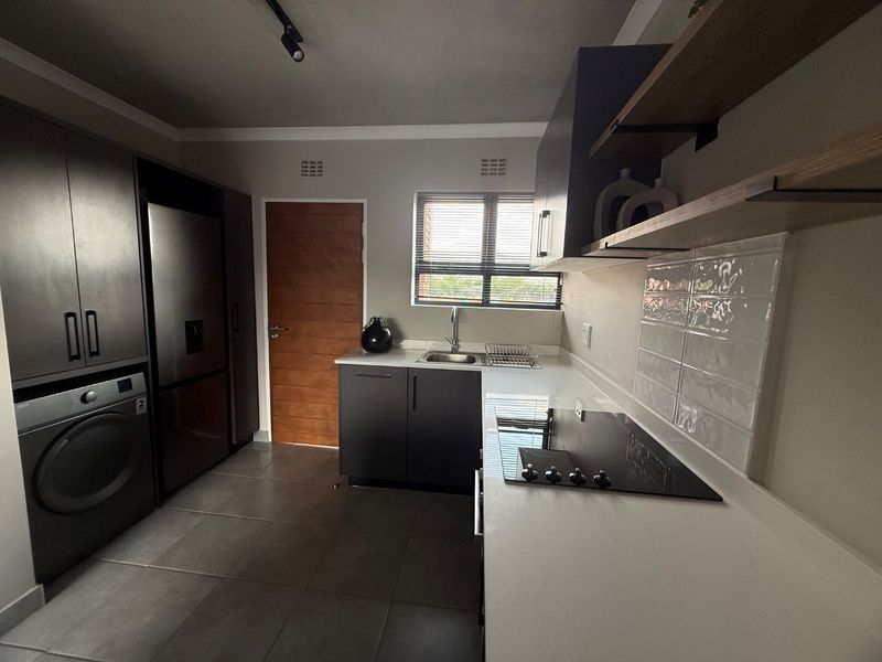 Modern kitchen featuring dark cabinetry, stone countertops, subway tile backsplash, integrated appliances, and sleek tiled flooring with ample natural light.