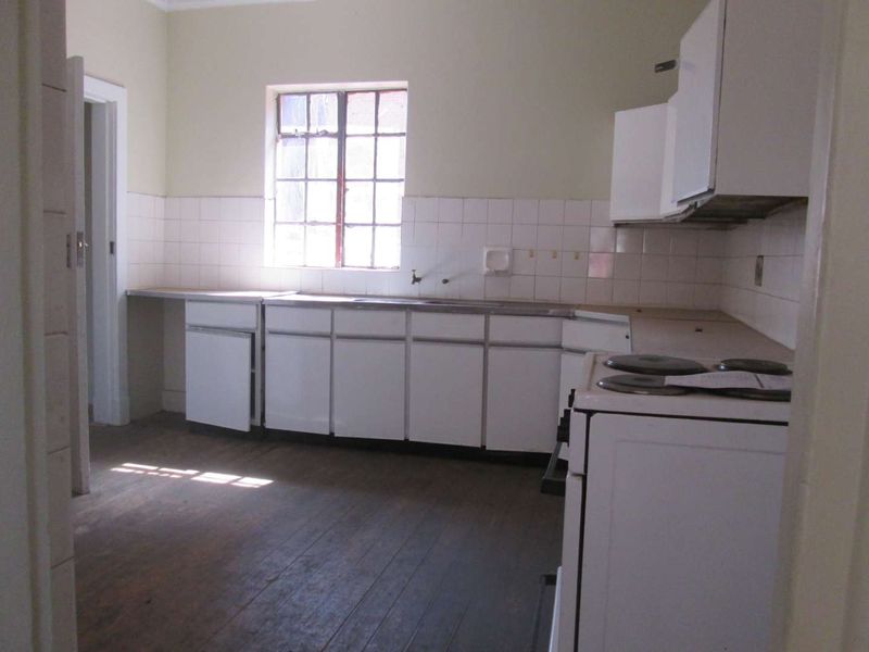 A dated, empty kitchen featuring original timber flooring, white cabinetry, a tiled backsplash, and a freestanding stove, offering significant potential for renovation.
