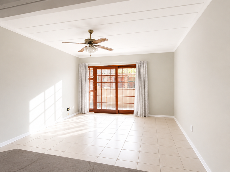 A bright, empty living room featuring neutral tiled flooring, a ceiling fan, and large sliding glass doors providing access to the exterior.