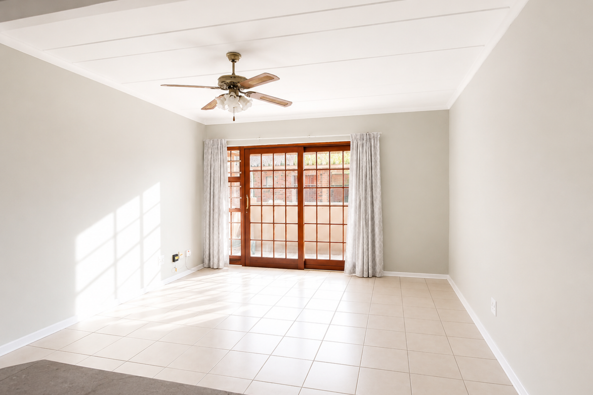 A bright, empty living room featuring neutral tiled flooring, a ceiling fan, and large sliding glass doors providing access to the exterior.
