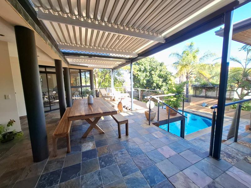 Spacious covered patio featuring slate tile flooring, a modern louvre roof system, and direct access to an integrated swimming pool area.