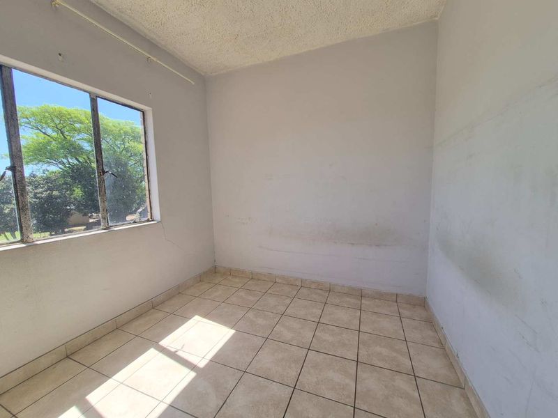 An empty bedroom featuring tiled flooring, a metal-framed window, and textured ceiling, requiring cosmetic updates to the wall finishes.