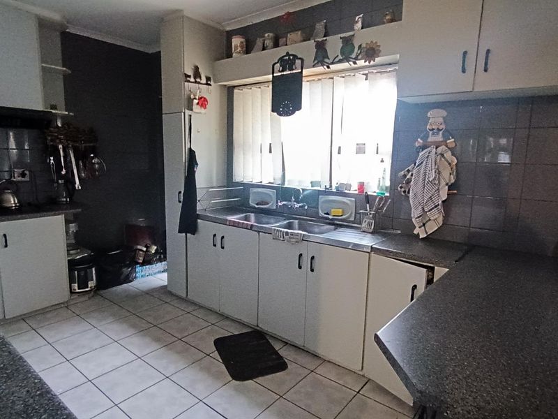 A functional kitchen featuring tiled flooring, laminate countertops, and a double basin sink with ample built-in cabinetry and tiled splashbacks.