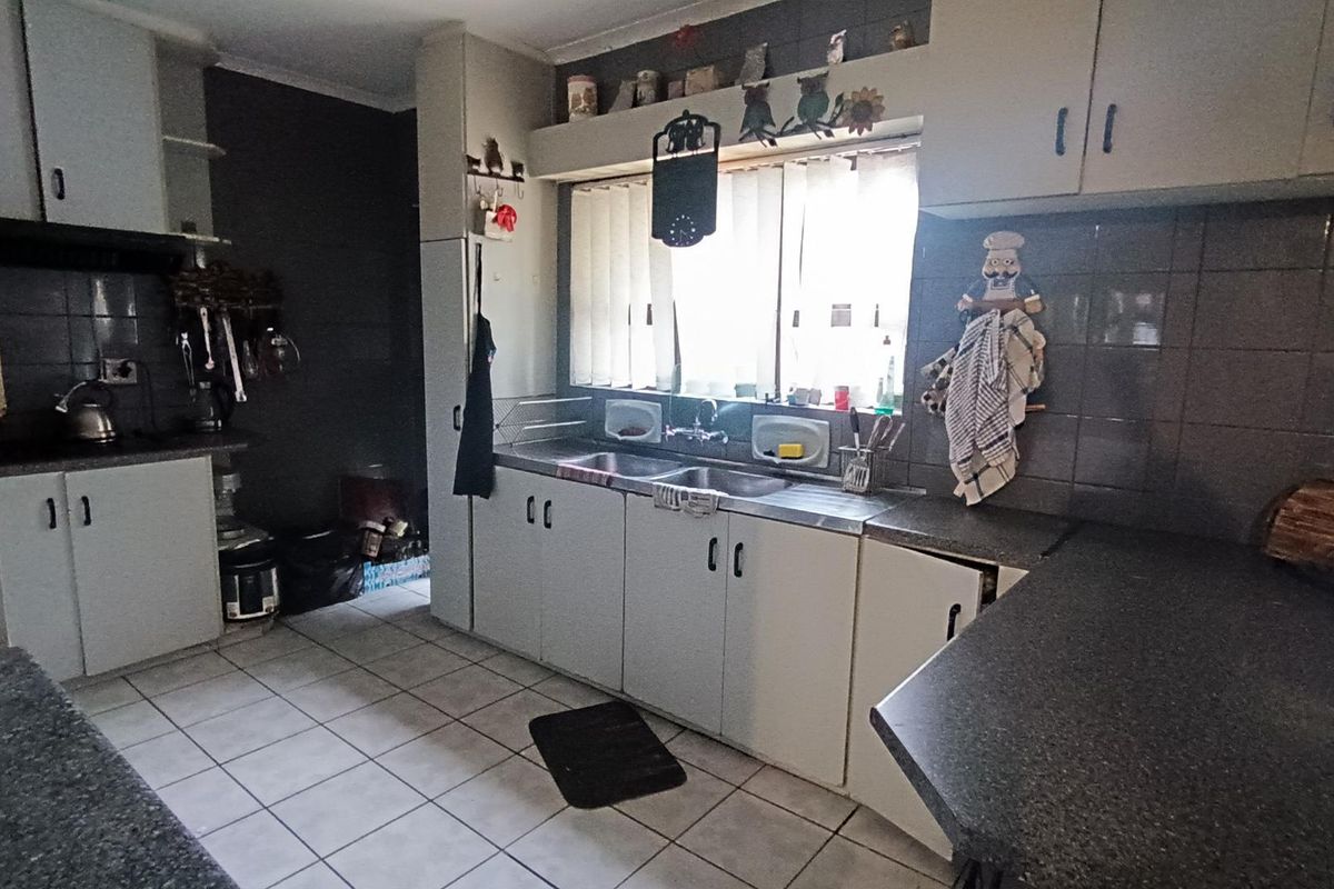 A functional kitchen featuring tiled flooring, laminate countertops, and a double basin sink with ample built-in cabinetry and tiled splashbacks.