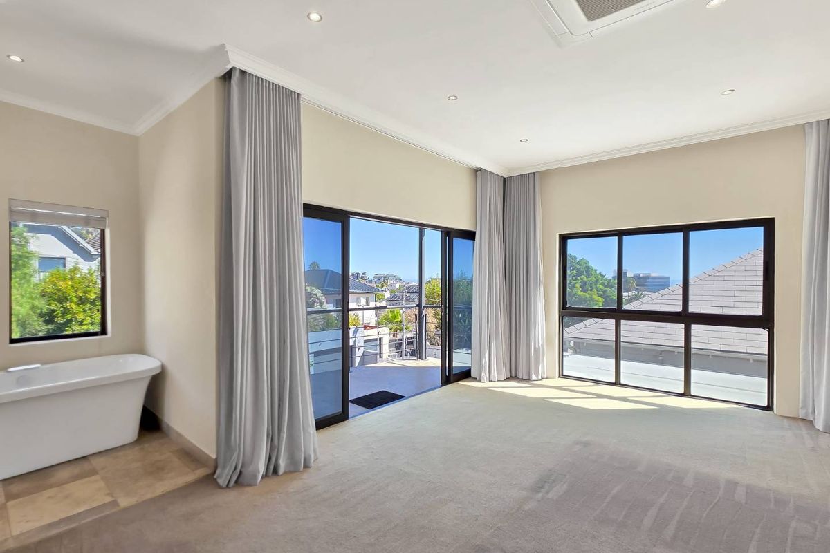Spacious bedroom featuring a freestanding bathtub, large windows, recessed ceiling lighting, and sliding glass doors opening onto a private balcony.