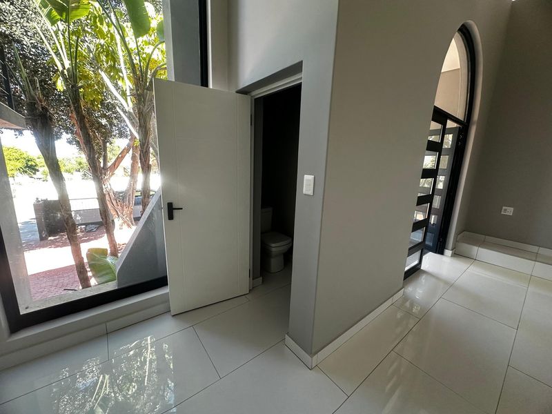 A bright, modern hallway featuring large floor-to-ceiling windows, polished porcelain tiles, and an arched entrance leading to a guest toilet.