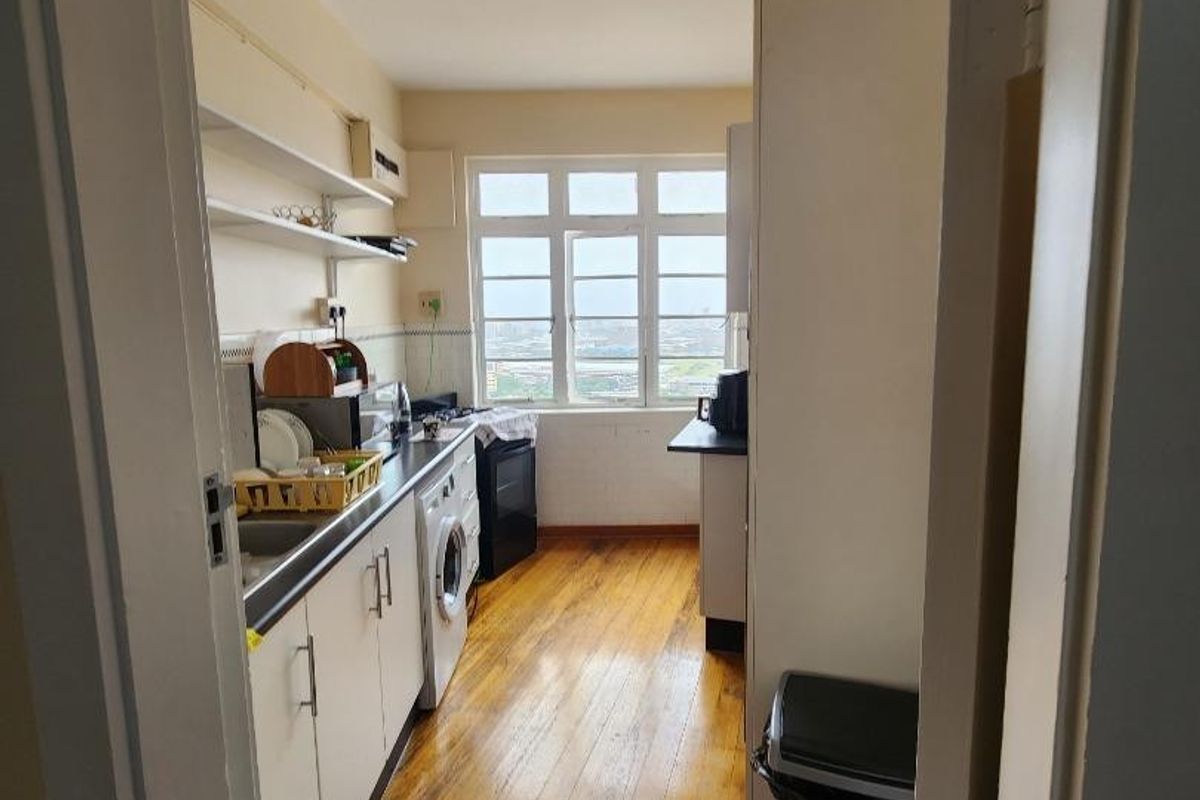 A functional galley-style kitchen featuring wooden flooring, built-in cabinetry, open shelving, and a window providing natural light.