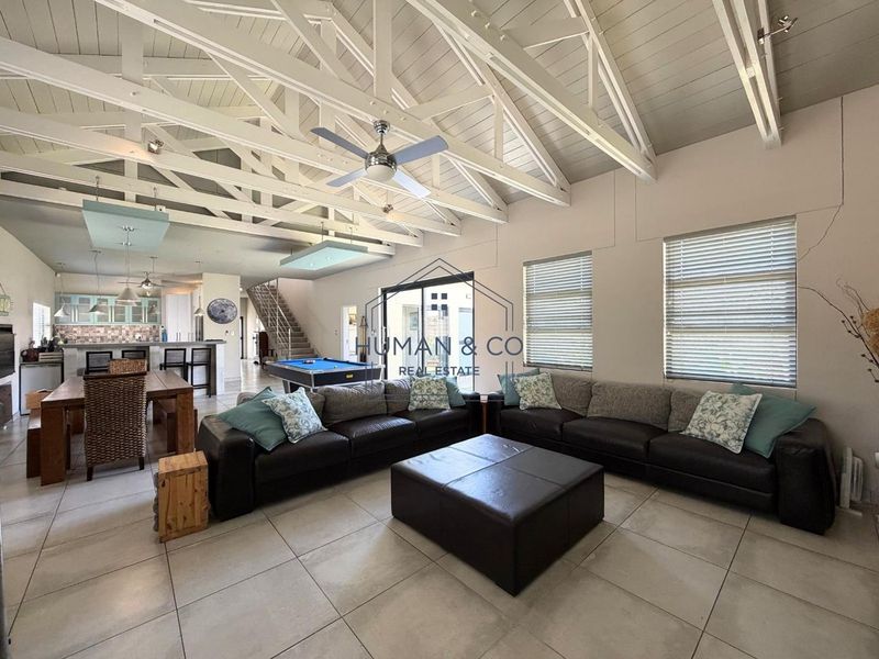 Spacious open-plan living area featuring high vaulted ceilings with exposed trusses, tiled floors, and a seamless flow to the kitchen and staircase.