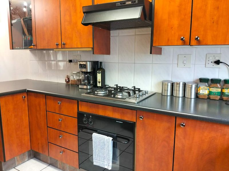A functional kitchen featuring warm-toned wooden cabinetry, dark laminate countertops, a built-in gas hob, oven, and a tiled backsplash.