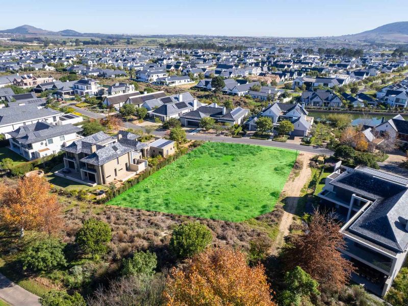 An aerial view of a vacant residential plot situated within a developed estate, surrounded by established homes and landscaped grounds.