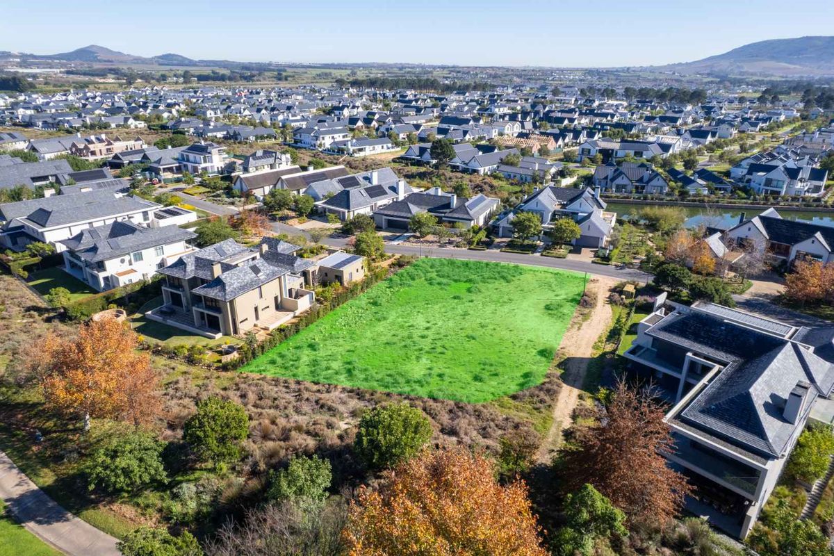 An aerial view of a vacant residential plot situated within a developed estate, surrounded by established homes and landscaped grounds.