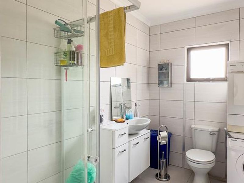 A functional bathroom featuring a glass shower enclosure, wall-mounted vanity with vessel sink, and tiled finishes throughout.