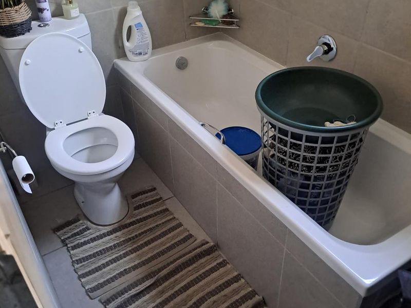 A functional bathroom featuring a standard toilet, a built-in bathtub with wall-mounted mixer tap, and neutral wall and floor tiling.