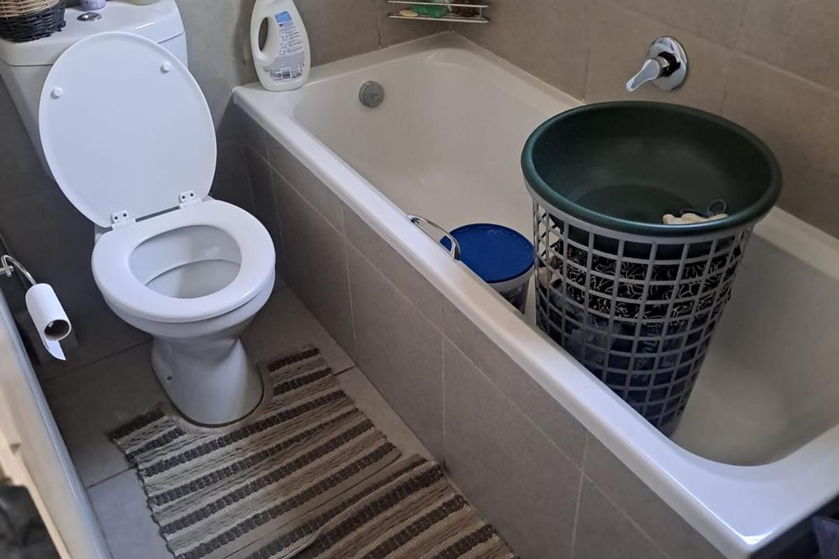 A functional bathroom featuring a standard toilet, a built-in bathtub with wall-mounted mixer tap, and neutral wall and floor tiling.