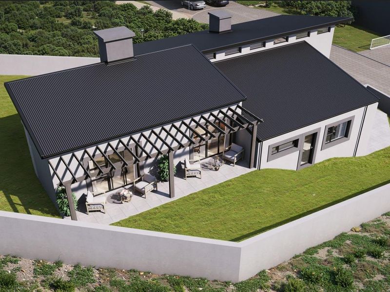 Aerial view of a modern house featuring a dark corrugated metal roof, a covered patio with a pergola, and a surrounding perimeter wall.
