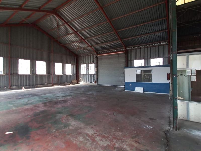 Spacious industrial warehouse featuring a high-clearance steel portal frame, concrete flooring, a large roller shutter door, and an integrated office partition.