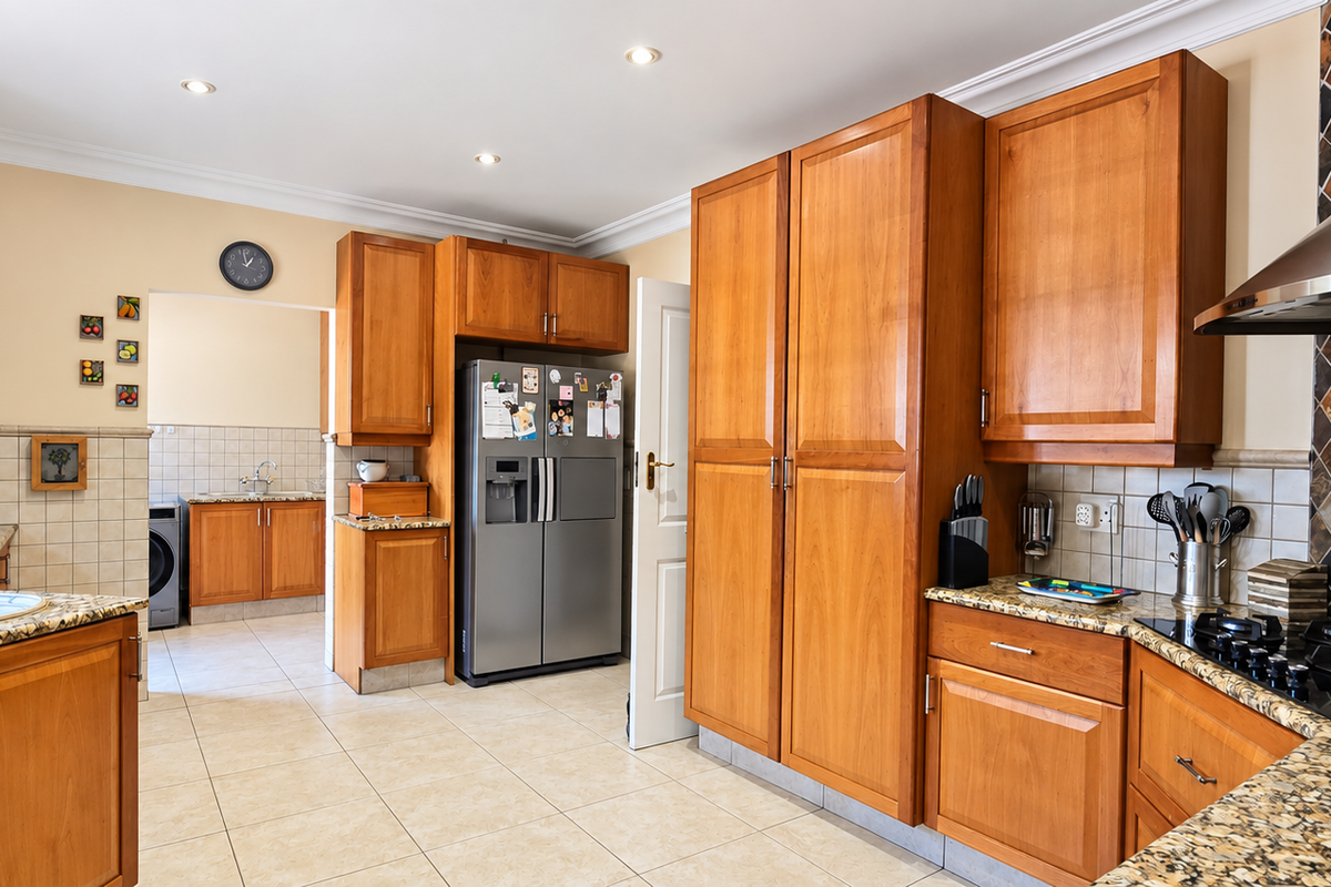 A well-maintained kitchen featuring warm wooden cabinetry, granite countertops, a gas hob with stainless steel extractor, and a separate scullery area.