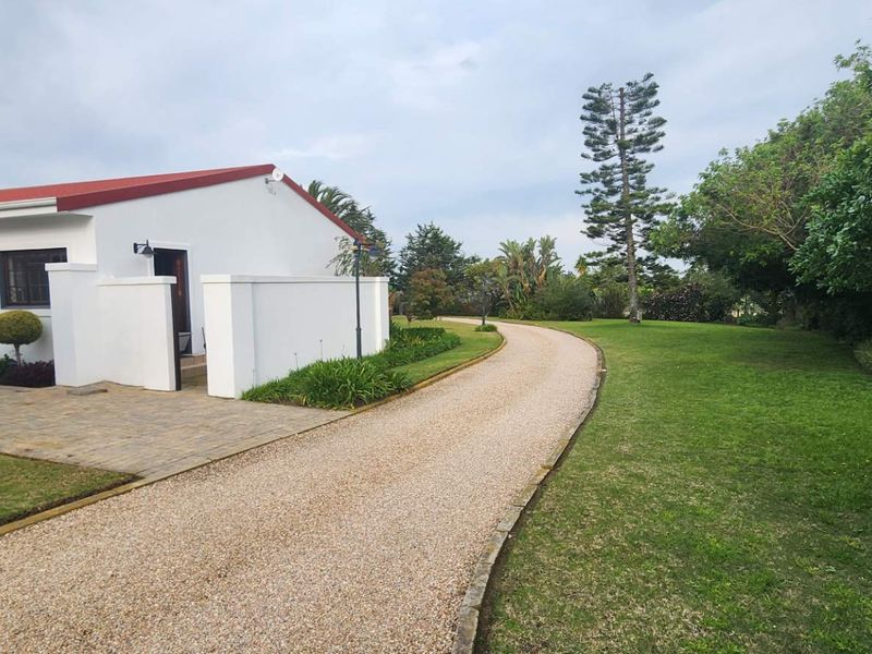 A well-maintained farm property featuring a gravel driveway leading to the main building with a red metal roof and landscaped garden surroundings.
