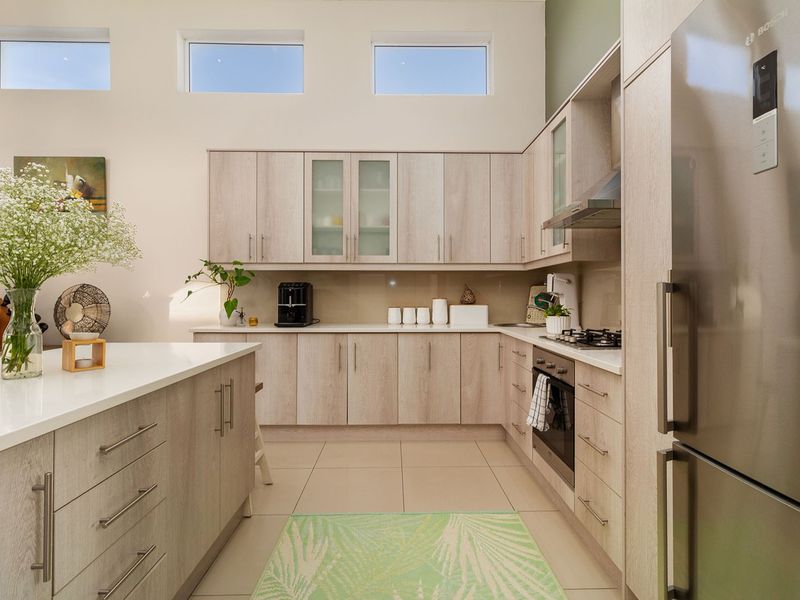 Modern kitchen featuring light wood-grain cabinetry, stone countertops, a central island, and high-level clerestory windows providing ample natural light.