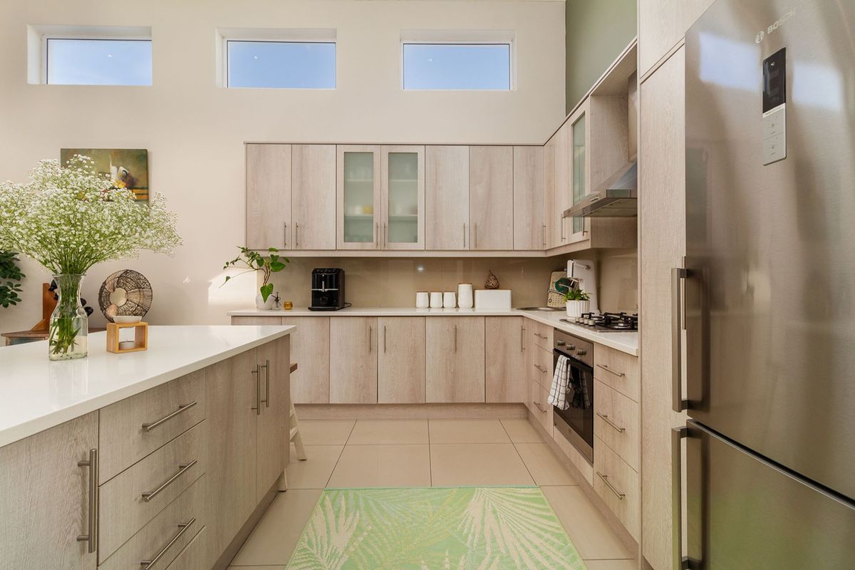 Modern kitchen featuring light wood-grain cabinetry, stone countertops, a central island, and high-level clerestory windows providing ample natural light.