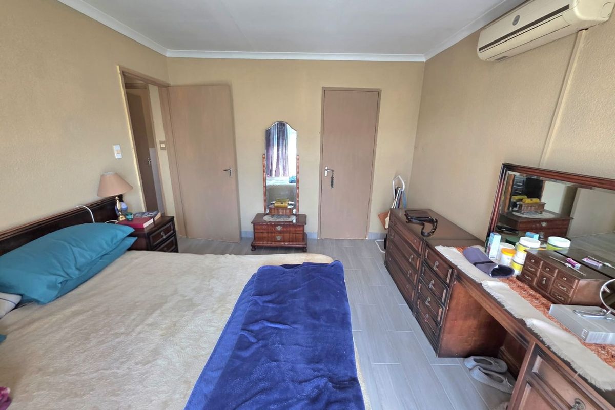 A functional bedroom featuring tiled flooring, a wall-mounted air conditioning unit, and neutral wall finishes.