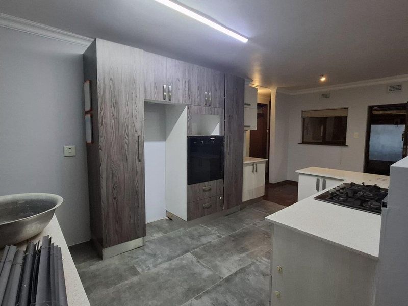A spacious kitchen featuring modern grey cabinetry, stone countertops, a built-in oven, and a gas hob, currently awaiting final finishing touches.