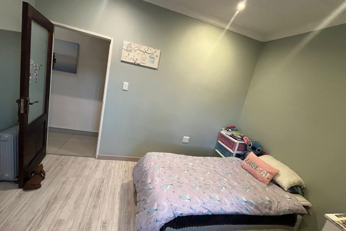 A bedroom featuring light-toned laminate flooring, soft green wall paint, and recessed ceiling lighting, providing a neutral base for interior design.