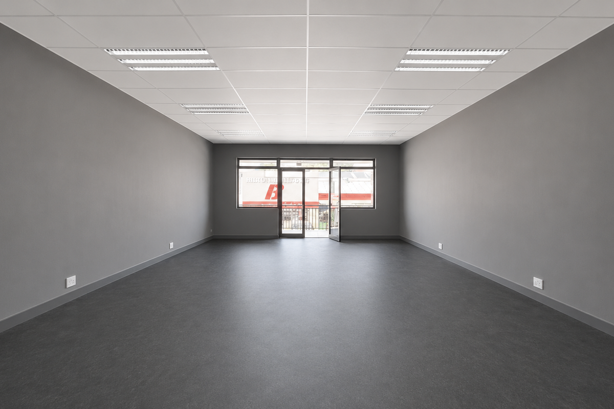 A spacious, modern, and empty office suite featuring a clean grey finish, suspended ceiling with recessed lighting, and large windows providing natural light.