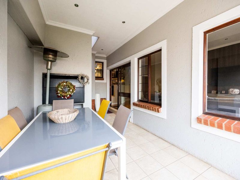 A covered patio area featuring tiled flooring, recessed downlights, and a built-in braai, providing a functional outdoor entertainment space.