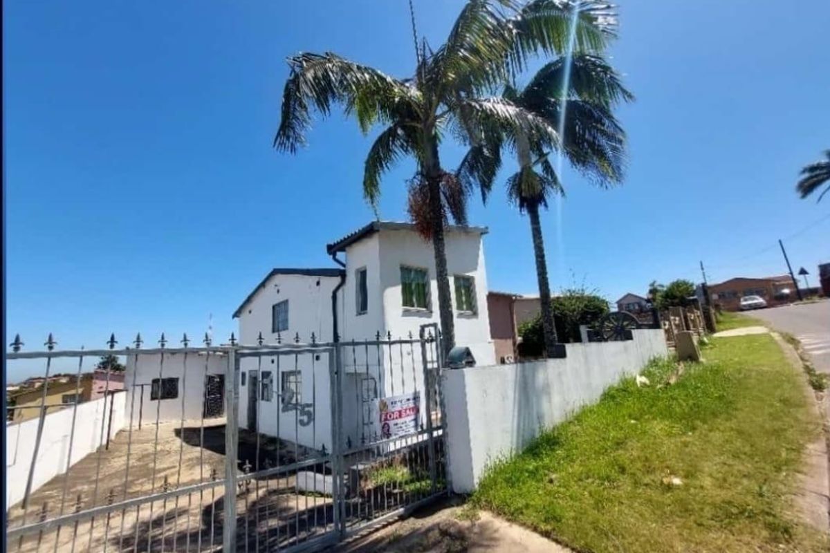 Front exterior view of a two-story house featuring a metal gated entrance, boundary wall, and established palm trees.