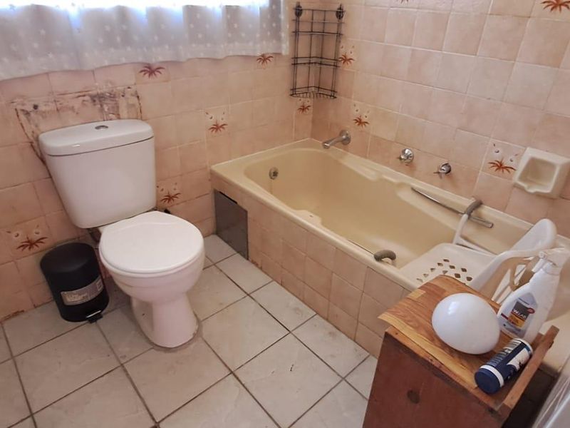 A dated bathroom featuring a built-in bathtub, toilet, and tiled finishes, requiring renovation to update the fixtures and wall surfaces.