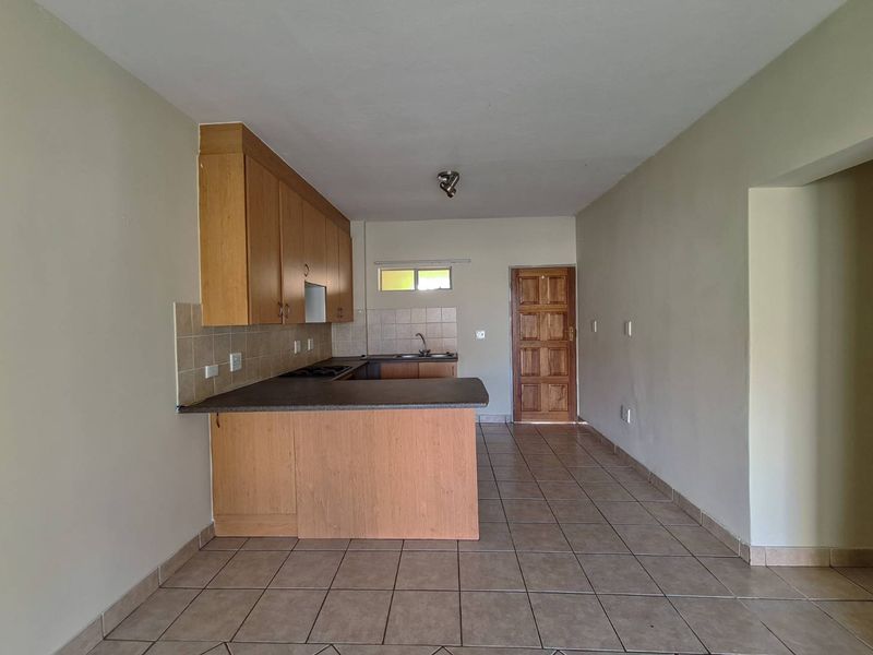 An open-plan kitchen and living area featuring tiled flooring, wooden cabinetry, and a functional layout, presented in a clean, vacant condition.