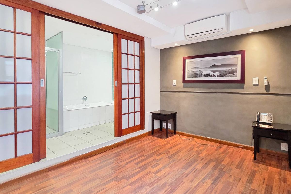 Spacious bedroom featuring timber flooring, split system air conditioning, and sliding timber doors providing direct access to an en-suite bathroom.