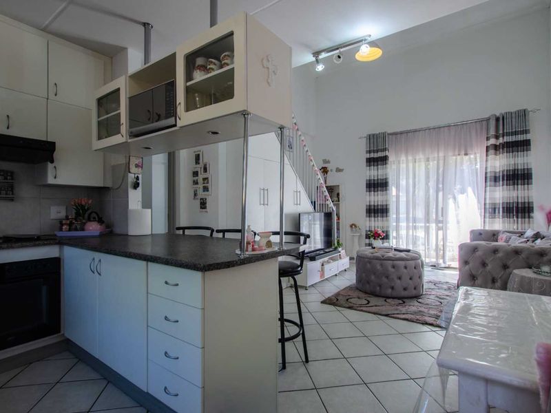 Open-plan living area featuring a functional kitchen with built-in cabinetry, a breakfast island, tiled flooring, and direct access to a patio through sliding doors.