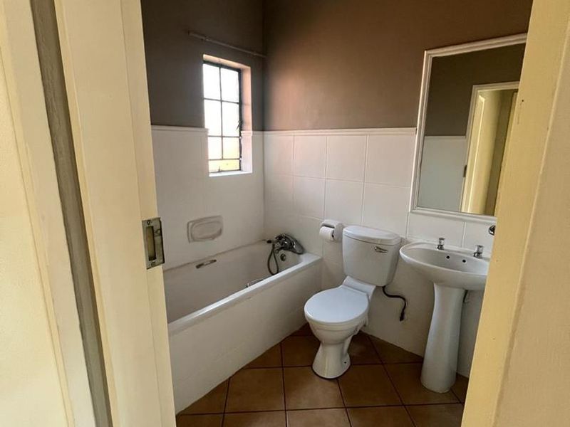 A functional bathroom featuring a bathtub, pedestal basin, and toilet with neutral wall tones and tiled flooring.