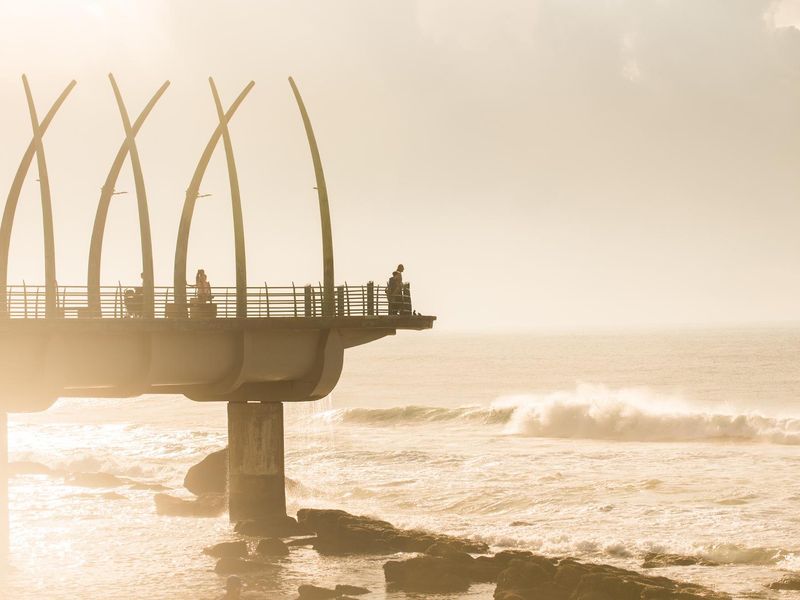 A scenic view of the iconic Umhlanga pier extending over the ocean at sunrise, highlighting the coastal location and architectural landmark.