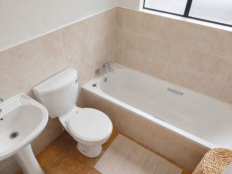 A functional bathroom featuring a pedestal basin, standard toilet, and a bathtub with tiled splashbacks and flooring.