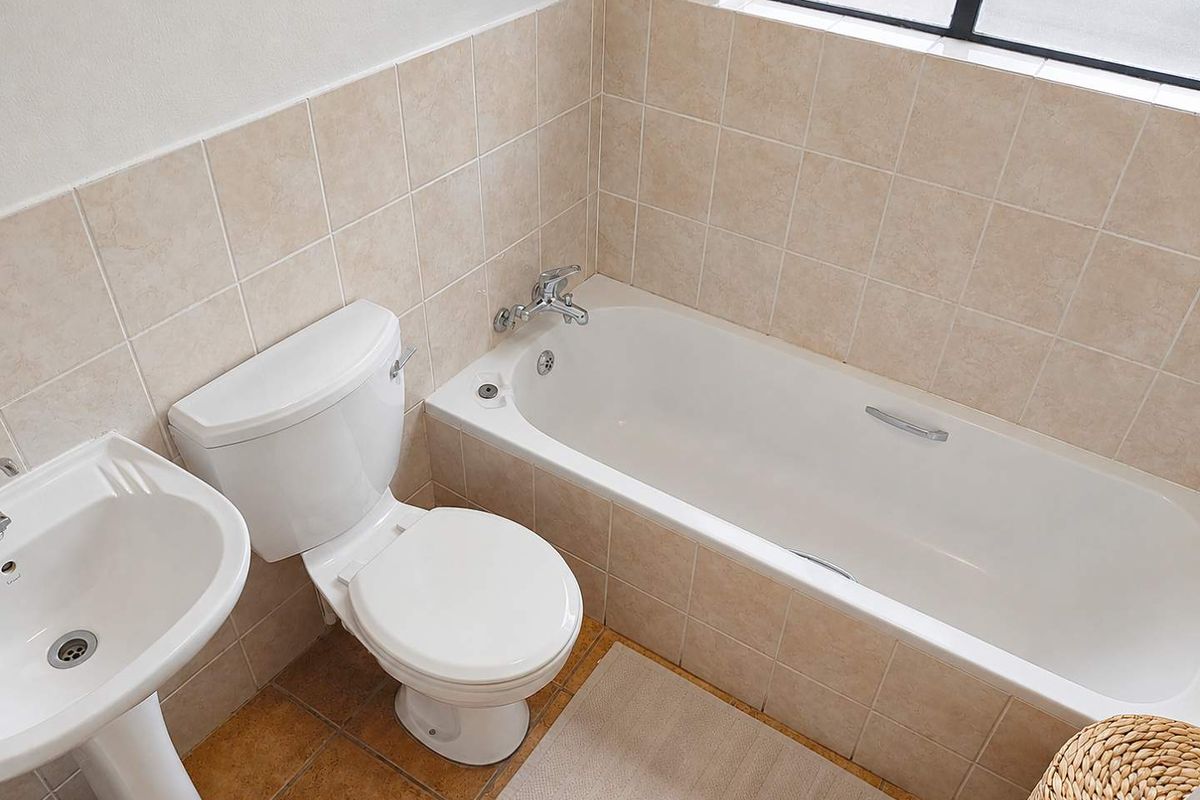 A functional bathroom featuring a pedestal basin, standard toilet, and a bathtub with tiled splashbacks and flooring.