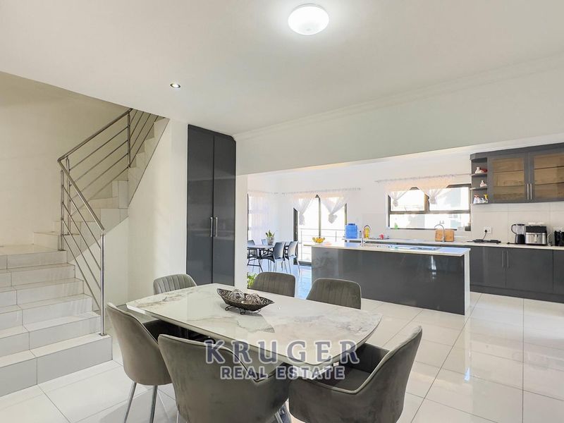 Spacious open-plan living area featuring a modern kitchen with island, tiled floors, and a contemporary staircase with stainless steel balustrade.