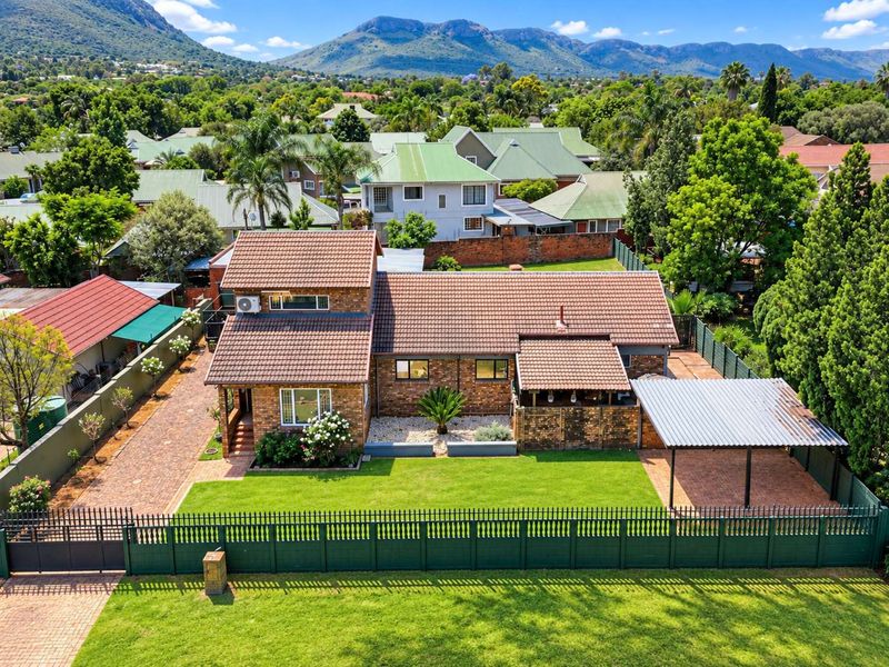 Aerial view of a well-maintained brick house featuring a tiled roof, paved driveway, carport, and established garden within a residential estate.