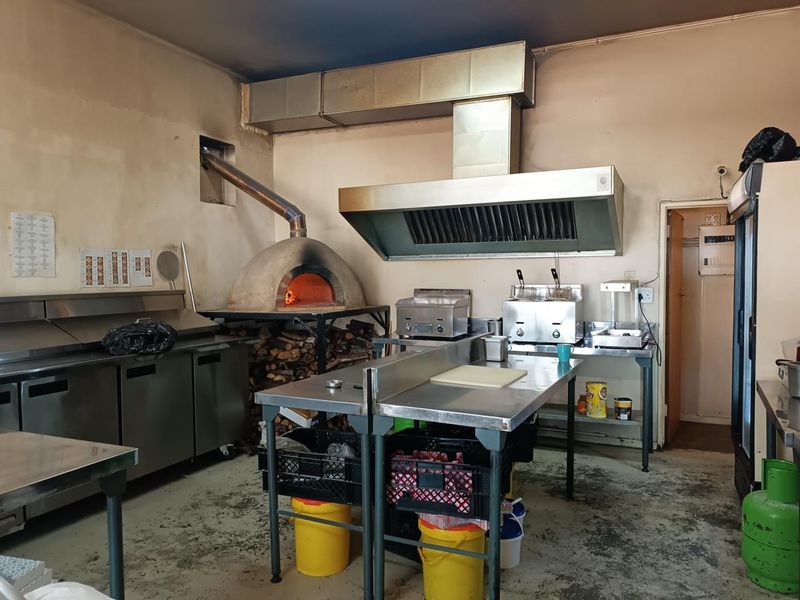 Commercial kitchen facility featuring a wood-fired pizza oven, stainless steel extraction system, prep counters, and commercial-grade cooking equipment.
