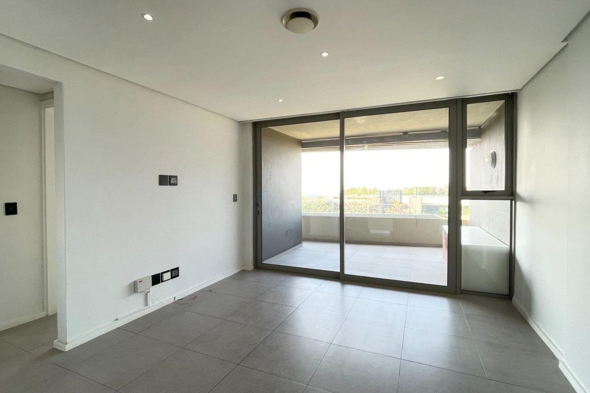 A bright, empty living area featuring large sliding glass doors that open onto a private balcony, finished with modern neutral floor tiles.