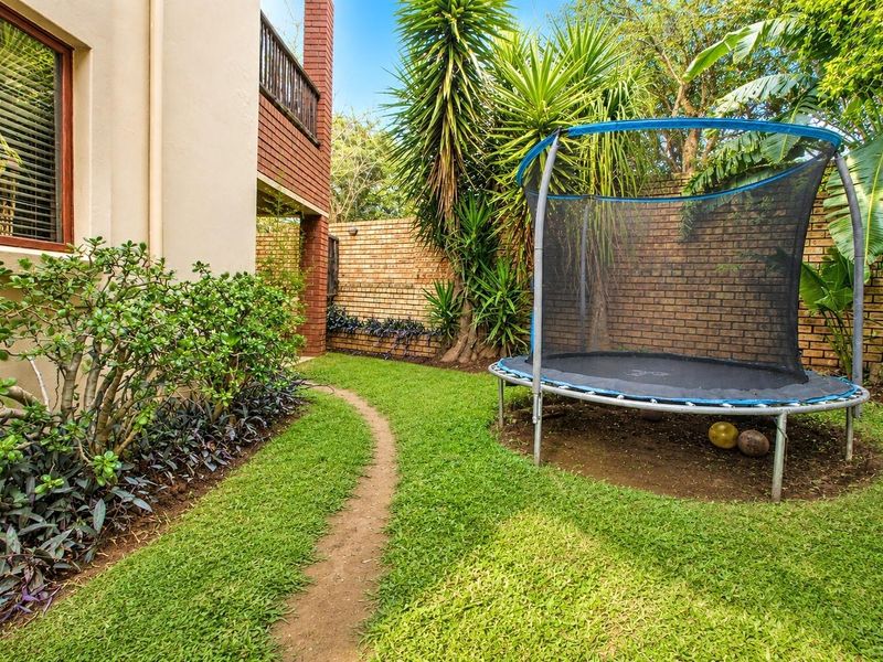 A private rear garden area featuring a lawn, established landscaping, and a brick boundary wall adjacent to the townhouse structure.