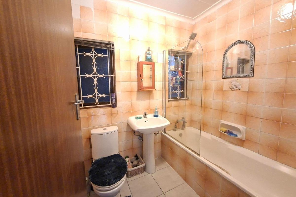 A functional bathroom featuring a pedestal basin, bathtub with a glass shower screen, and tiled finishes throughout.