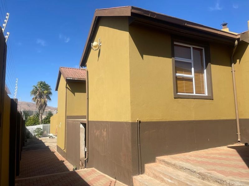 Rear exterior view of the property featuring a paved walkway, concrete steps, and painted exterior walls with downpipe infrastructure.
