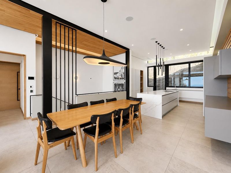Modern open-plan living and dining area featuring a sleek kitchen island, high-end finishes, timber ceiling accents, and abundant natural light.