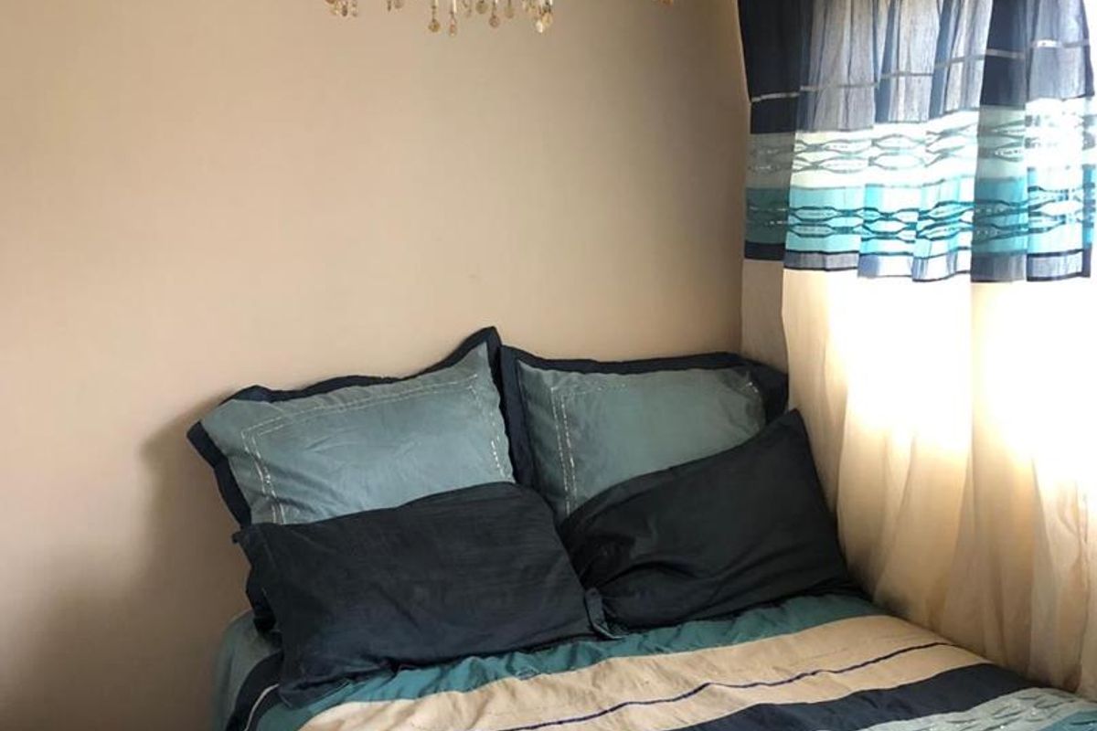A compact bedroom featuring a decorative crystal chandelier and natural light from the side window.
