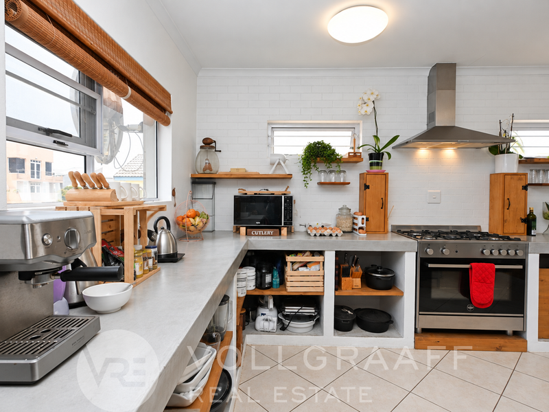 A functional kitchen featuring concrete countertops, a stainless steel gas stove with extractor fan, and open shelving with a clean, modern aesthetic.