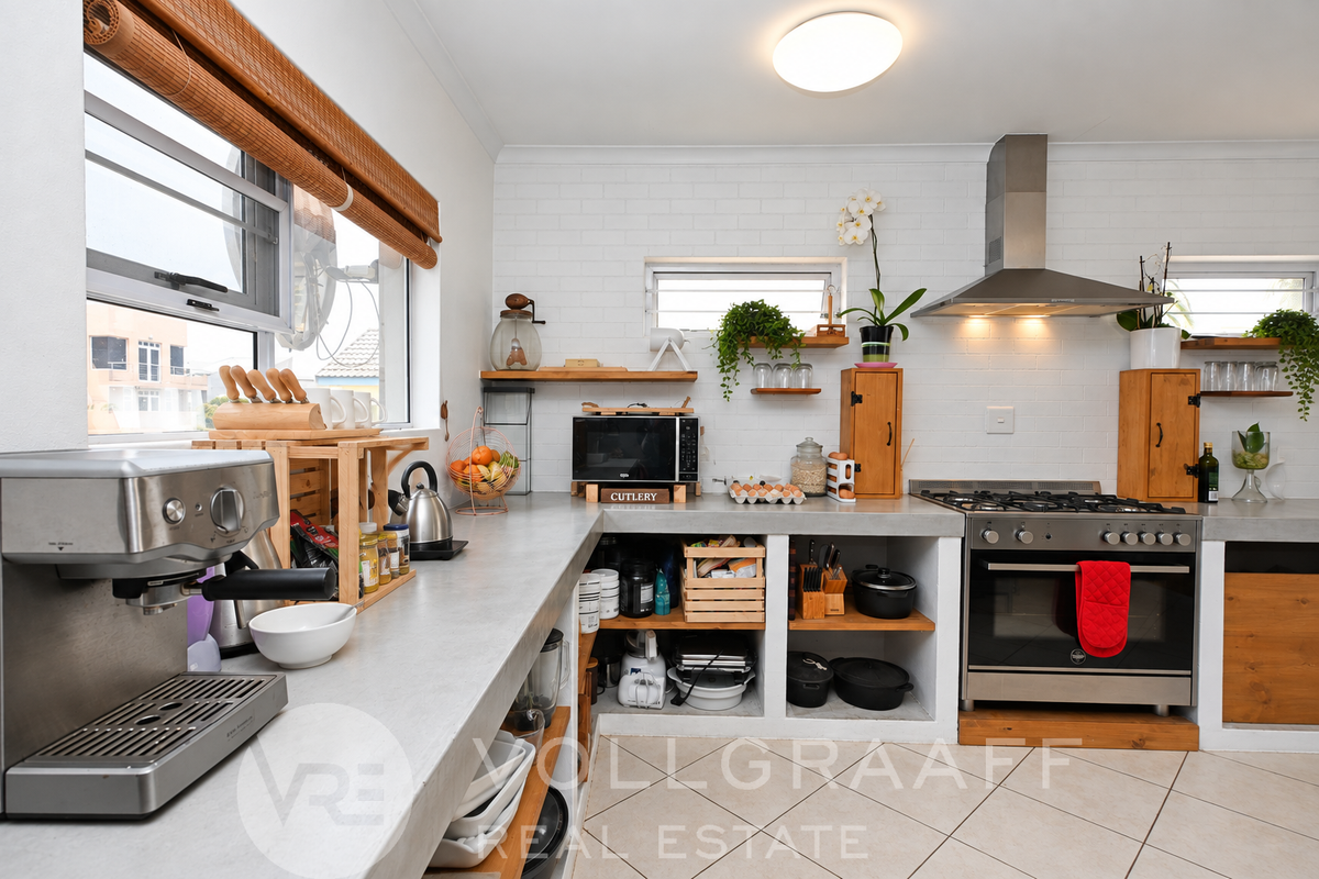 A functional kitchen featuring concrete countertops, a stainless steel gas stove with extractor fan, and open shelving with a clean, modern aesthetic.