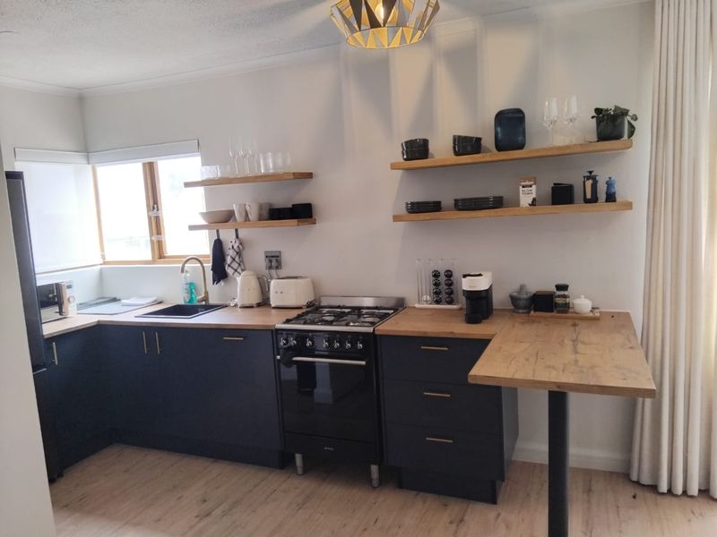 Modern kitchen featuring dark cabinetry, wooden countertops, floating shelves, a gas stove, and an integrated breakfast bar area.